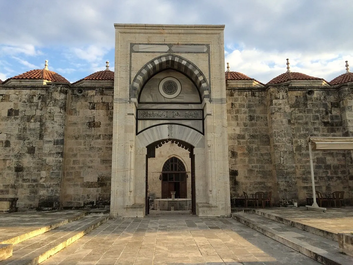 The courtyard and marble portal of the Grand Mosque of Tarsus, flanked by stone walls with red-tiled domes
