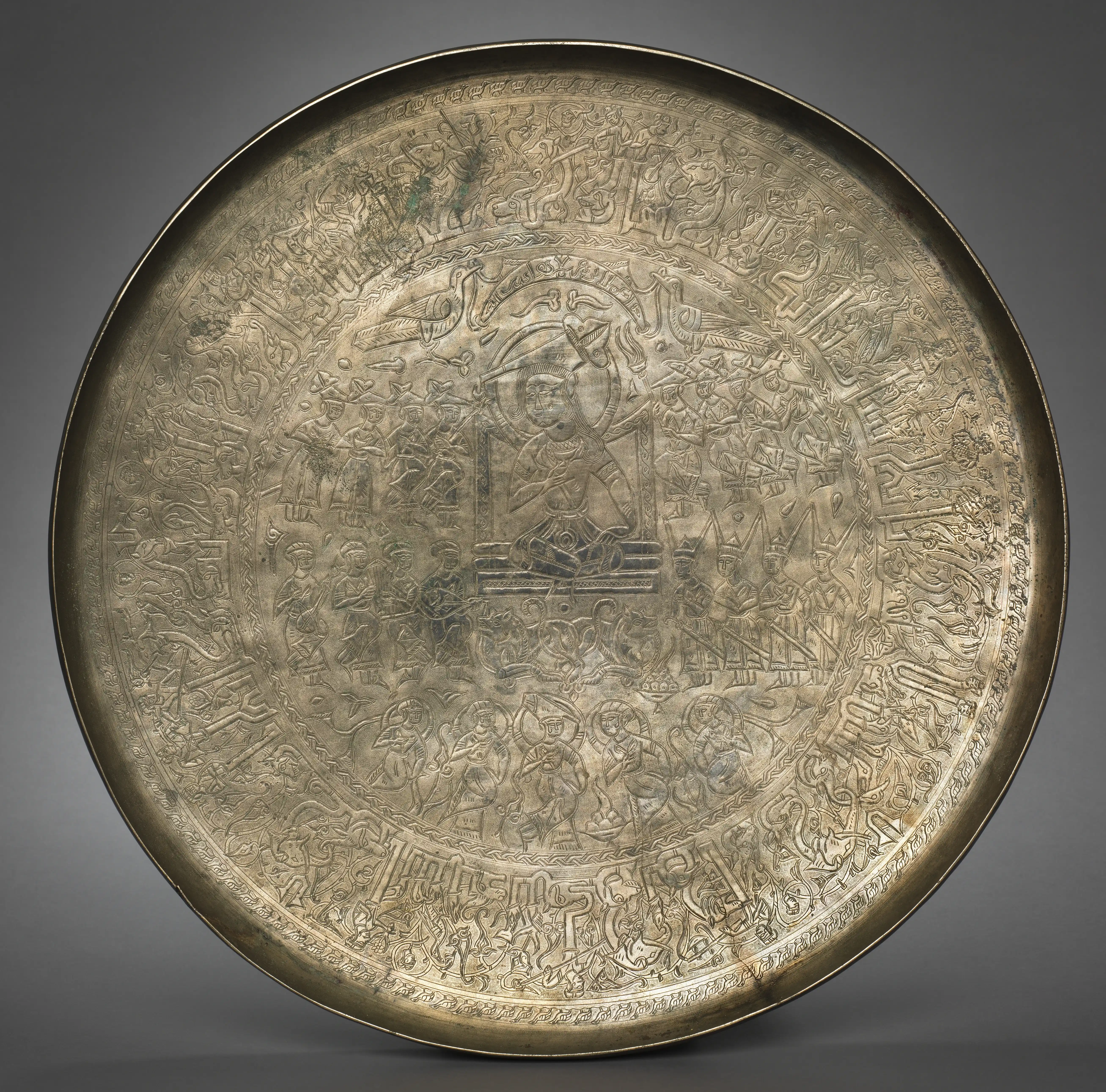 A large engraved brass salver, its centre showing an enthroned ruler seated cross-legged among courtiers, attendants and musicians, ringed by bands of Arabic inscription and figural ornament