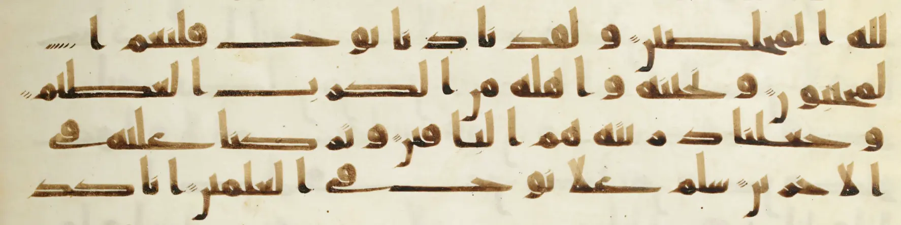 Four lines of early angular Kufic Arabic script in brown ink on parchment, with sparse red vowel marks