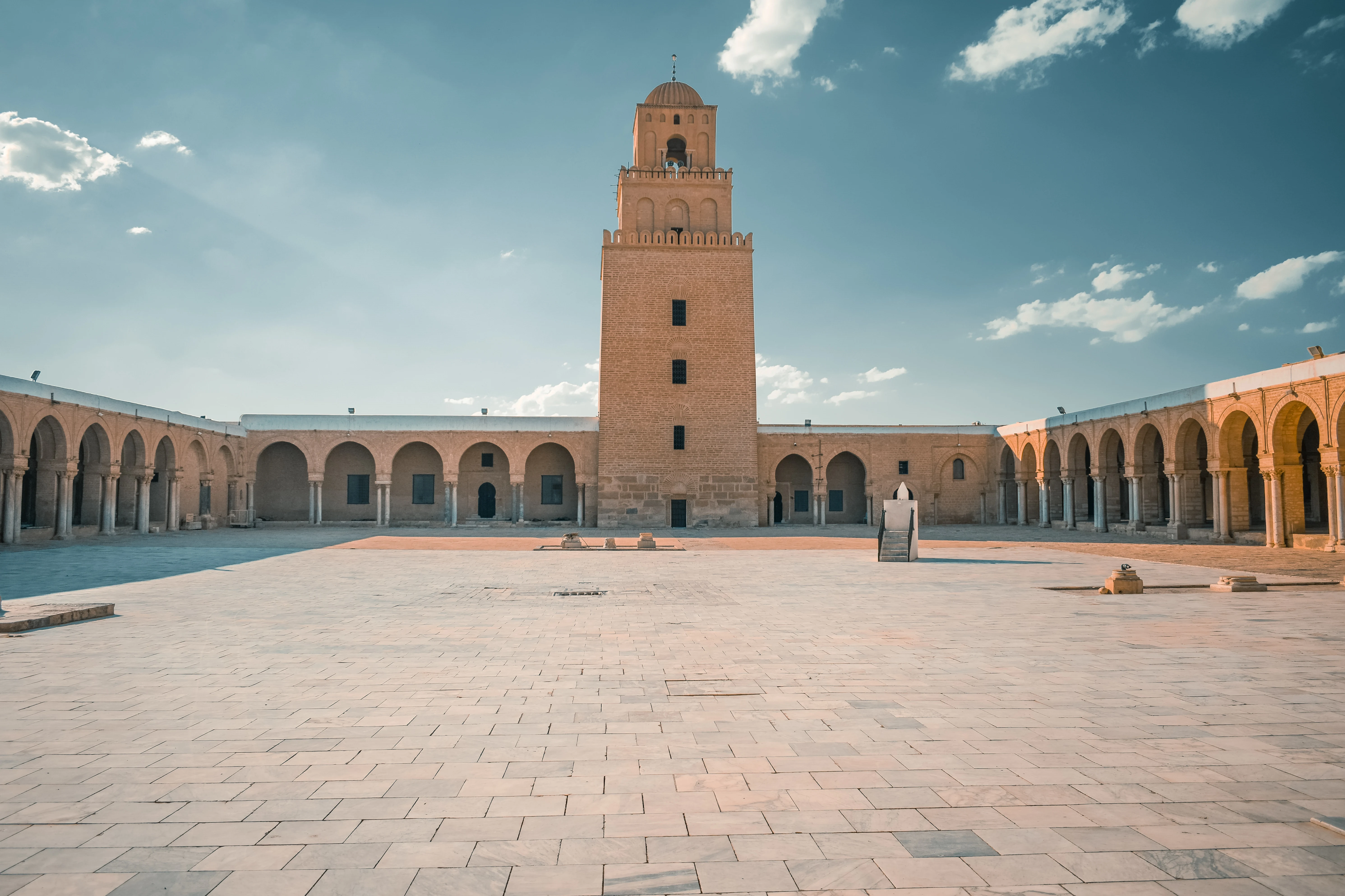 The tall, tapering square minaret of the Great Mosque of Kairouan, built in receding tiers, seen from the courtyard with its arcaded gallery running alongside